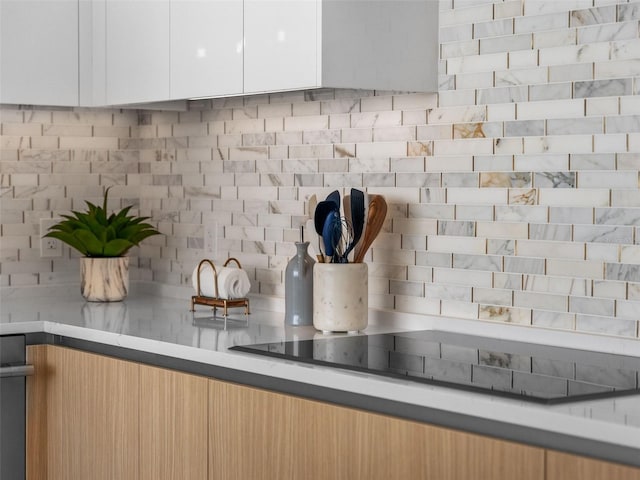 interior details with black electric stovetop, white cabinets, light countertops, tasteful backsplash, and modern cabinets