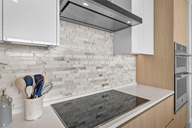 kitchen with light stone counters, tasteful backsplash, light brown cabinets, modern cabinets, and wall chimney exhaust hood