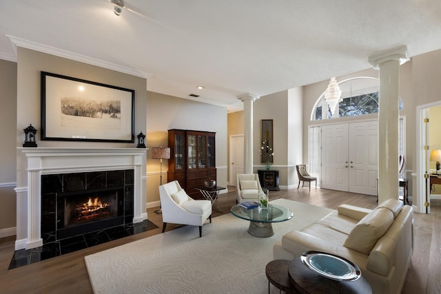 living area featuring a tile fireplace, wood finished floors, baseboards, ornamental molding, and ornate columns