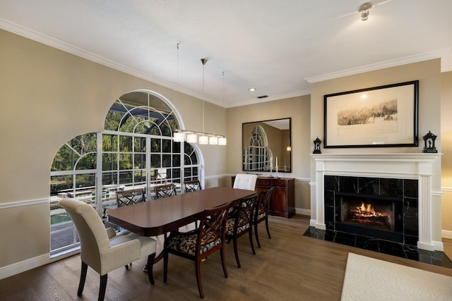 dining space featuring baseboards, ornamental molding, a tiled fireplace, and wood finished floors