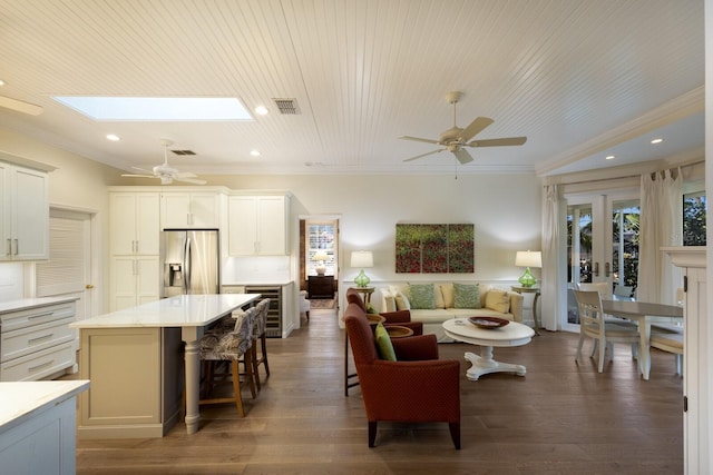 living area with a skylight, visible vents, ornamental molding, ceiling fan, and wood finished floors