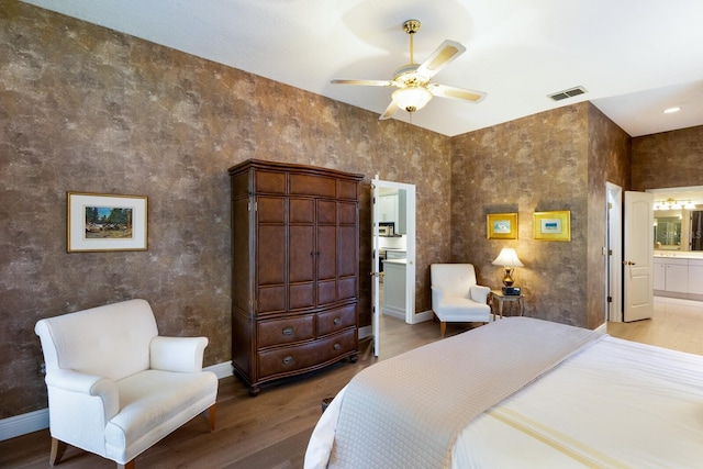 bedroom with wood finished floors, ensuite bath, visible vents, and baseboards