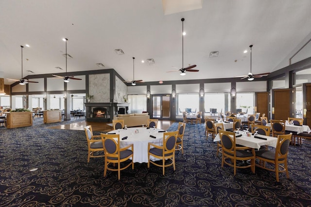 carpeted dining room featuring high vaulted ceiling, visible vents, and a lit fireplace