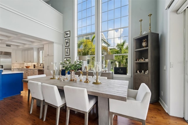 dining room with a towering ceiling, a healthy amount of sunlight, coffered ceiling, and light hardwood / wood-style floors