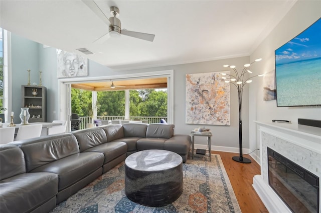 living room featuring wood-type flooring, a stone fireplace, and ceiling fan