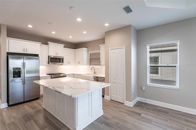 kitchen with white cabinetry, light stone counters, light wood-type flooring, a kitchen island, and stainless steel appliances