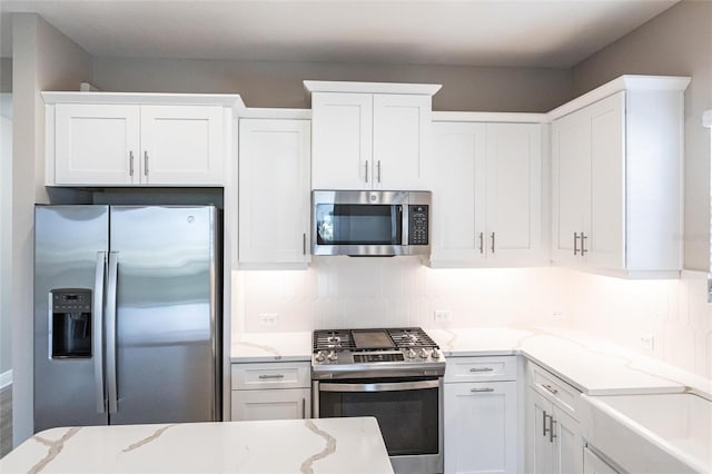 kitchen with appliances with stainless steel finishes, white cabinets, light stone counters, and decorative backsplash