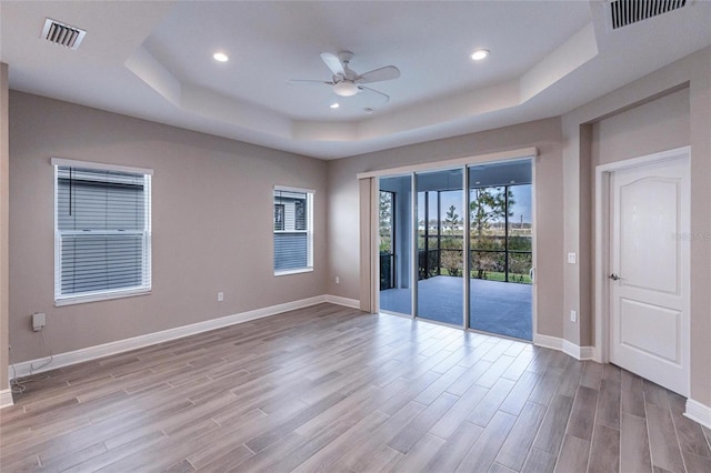 unfurnished room featuring a raised ceiling, ceiling fan, and light hardwood / wood-style floors