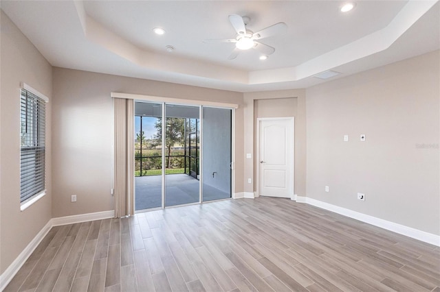 unfurnished bedroom with light hardwood / wood-style flooring, a tray ceiling, access to outside, and ceiling fan