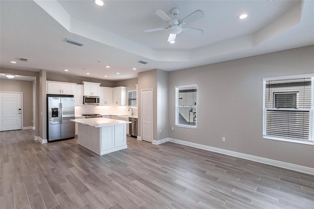 kitchen featuring white cabinetry, a center island, a tray ceiling, stainless steel appliances, and light wood-type flooring