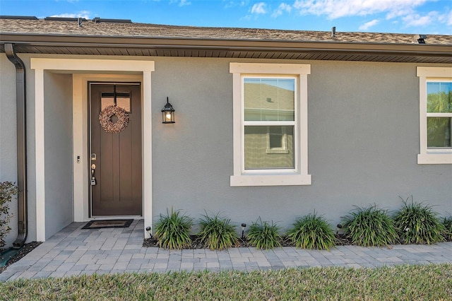 doorway to property with roof with shingles and stucco siding