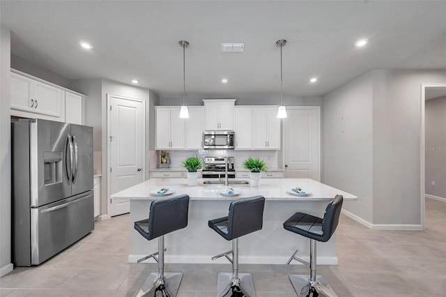 kitchen featuring stainless steel appliances, an island with sink, white cabinets, and decorative light fixtures