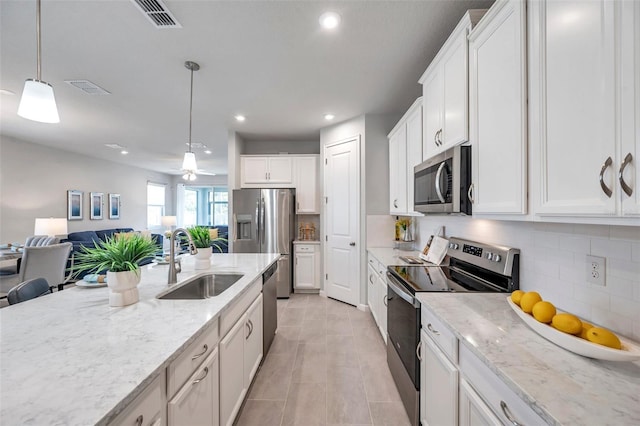 kitchen with sink, white cabinetry, light stone counters, appliances with stainless steel finishes, and pendant lighting