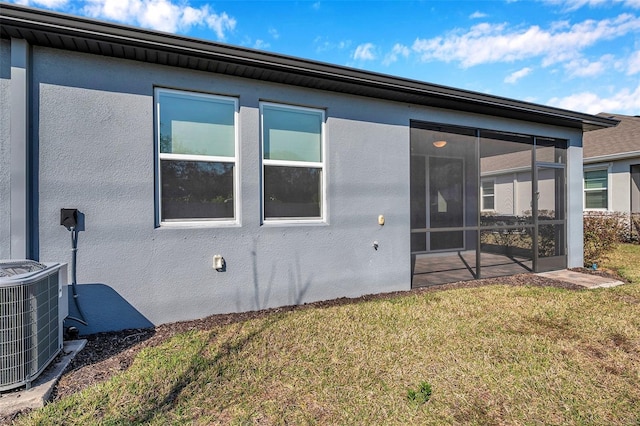 back of property with a yard, stucco siding, a sunroom, and central air condition unit