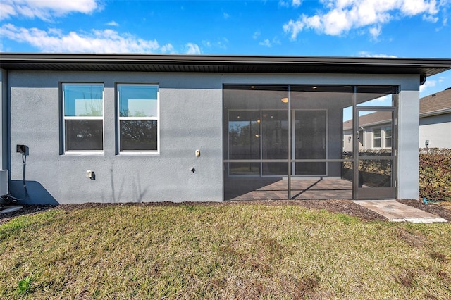 rear view of property with a sunroom, a lawn, and stucco siding