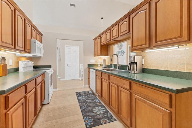 kitchen with tasteful backsplash, white appliances, sink, and light hardwood / wood-style flooring