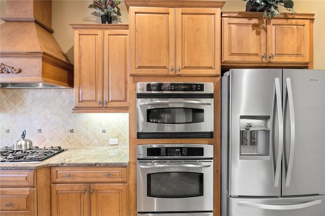 kitchen with light stone counters, decorative backsplash, custom range hood, and appliances with stainless steel finishes