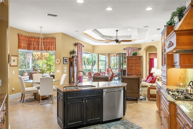 kitchen with sink, light stone counters, a center island with sink, appliances with stainless steel finishes, and a tray ceiling