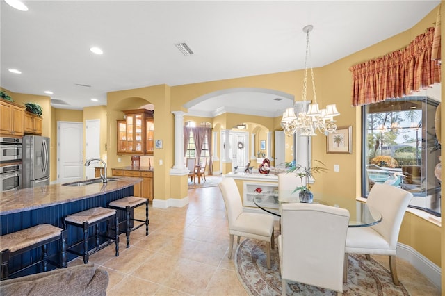 dining area with sink, light tile patterned floors, a notable chandelier, and ornate columns