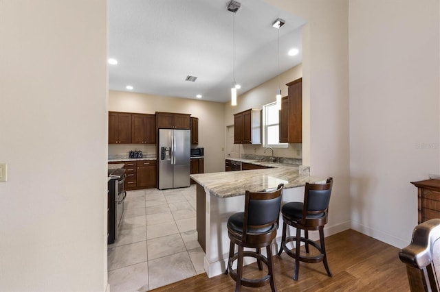 kitchen featuring a breakfast bar, decorative light fixtures, light stone counters, kitchen peninsula, and stainless steel appliances