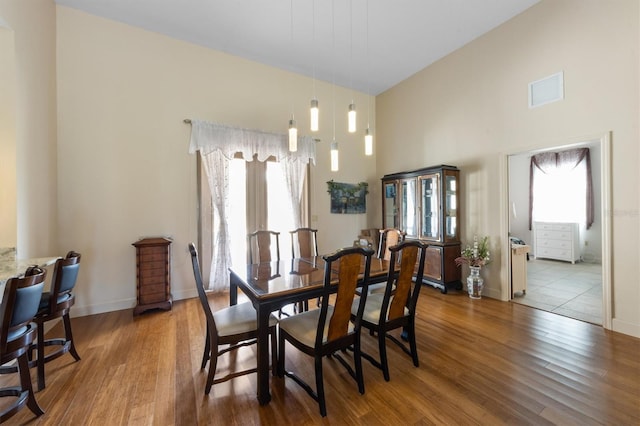 dining space with hardwood / wood-style floors, a towering ceiling, and a wealth of natural light