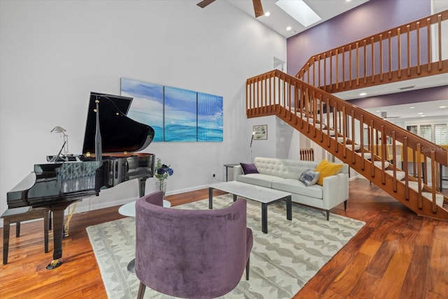 living room featuring hardwood / wood-style flooring, a skylight, ceiling fan, and a towering ceiling