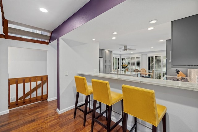 kitchen featuring stainless steel refrigerator, a breakfast bar, gray cabinetry, dark hardwood / wood-style floors, and kitchen peninsula