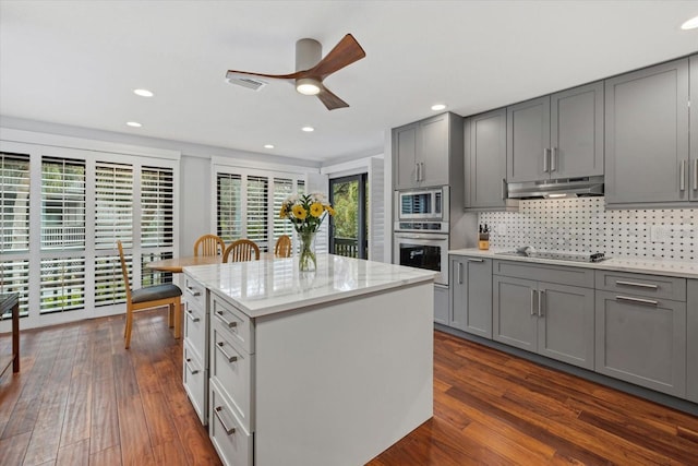 kitchen featuring gray cabinets, a kitchen island, decorative backsplash, stainless steel appliances, and a healthy amount of sunlight