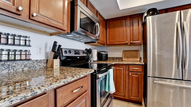 kitchen with light stone counters, stainless steel appliances, a textured ceiling, and light tile patterned floors