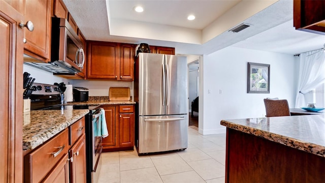 kitchen featuring light tile patterned floors, a tray ceiling, light stone countertops, and appliances with stainless steel finishes