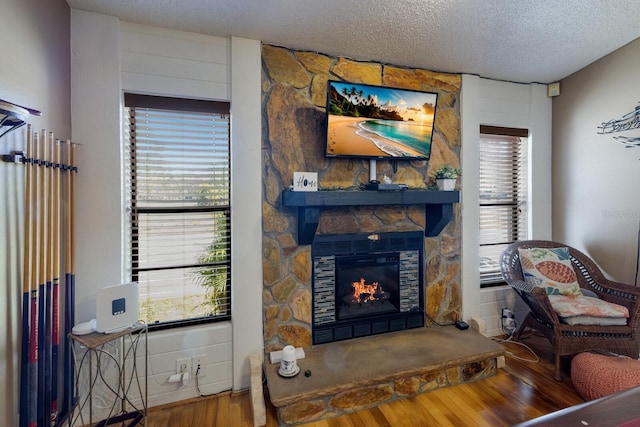 living room with hardwood / wood-style flooring, a stone fireplace, and a textured ceiling