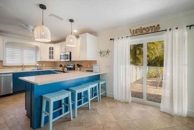 kitchen with appliances with stainless steel finishes, white cabinetry, sink, backsplash, and hanging light fixtures