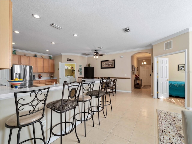 kitchen featuring light tile patterned flooring, ornamental molding, stainless steel fridge, kitchen peninsula, and ceiling fan