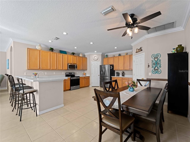 kitchen featuring light tile patterned flooring, crown molding, a textured ceiling, appliances with stainless steel finishes, and a kitchen island with sink