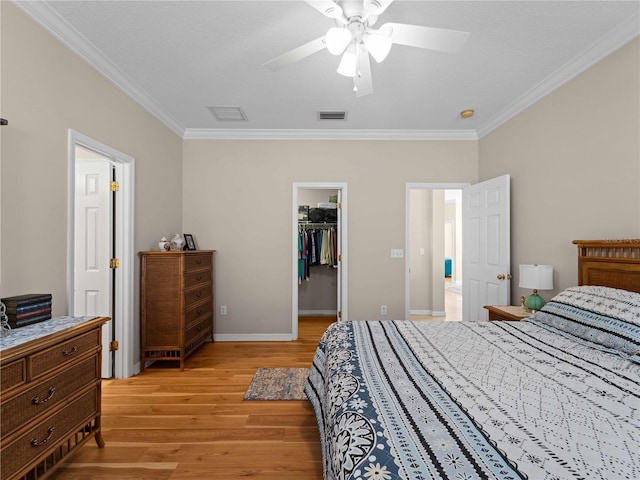 bedroom with a spacious closet, ceiling fan, light hardwood / wood-style floors, crown molding, and a closet