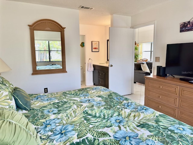 bedroom with ensuite bathroom, light tile patterned floors, and a textured ceiling