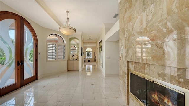 tiled entryway with french doors, a fireplace, and crown molding