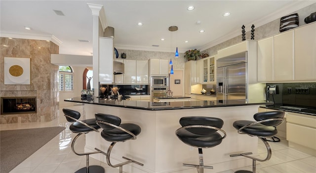 kitchen with a breakfast bar, crown molding, built in appliances, kitchen peninsula, and pendant lighting