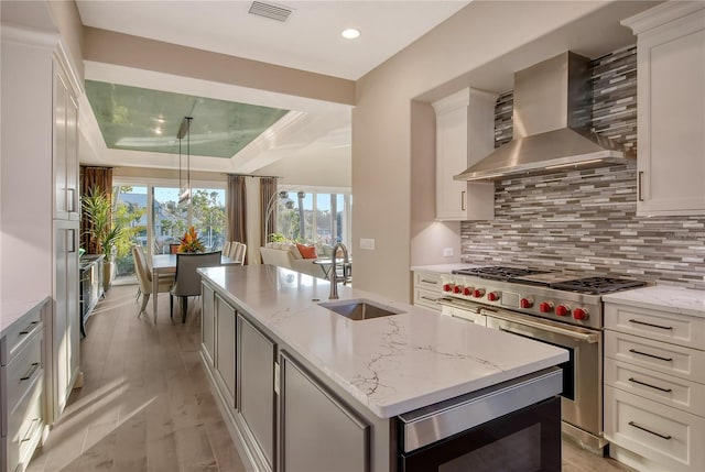 kitchen featuring sink, double oven range, light stone countertops, a center island with sink, and wall chimney exhaust hood