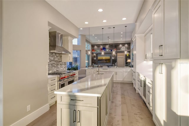 kitchen with wall chimney exhaust hood, hanging light fixtures, double oven range, kitchen peninsula, and white cabinets