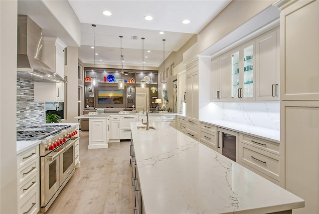 kitchen featuring pendant lighting, light stone countertops, kitchen peninsula, wall chimney exhaust hood, and range with two ovens