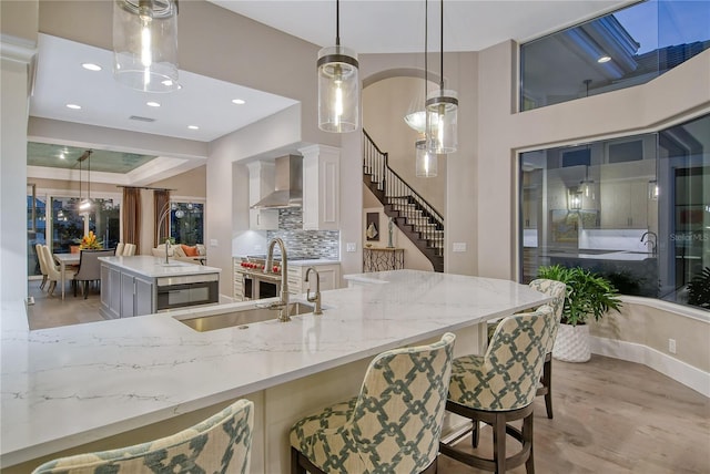 kitchen with a kitchen island, decorative light fixtures, sink, a kitchen breakfast bar, and wall chimney range hood