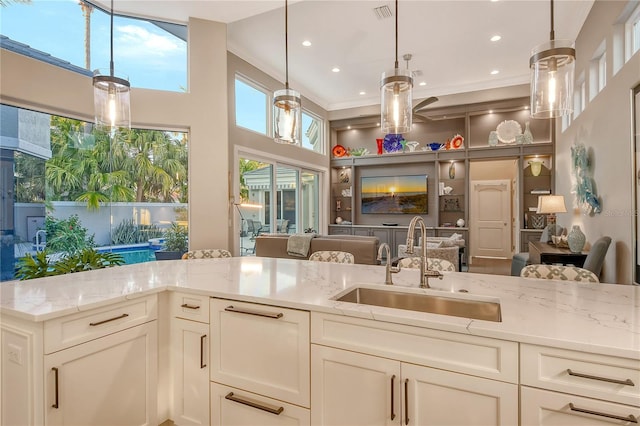 kitchen with pendant lighting, sink, a high ceiling, light stone counters, and crown molding