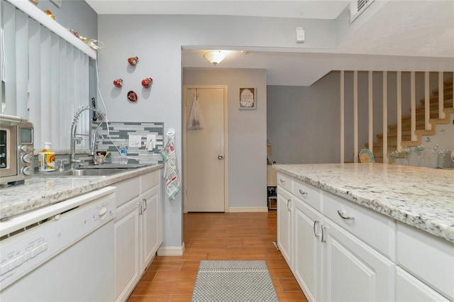 kitchen featuring dishwasher, white cabinetry, backsplash, light stone countertops, and light wood-type flooring