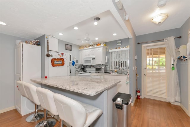 kitchen featuring white appliances, kitchen peninsula, white cabinets, and a kitchen bar