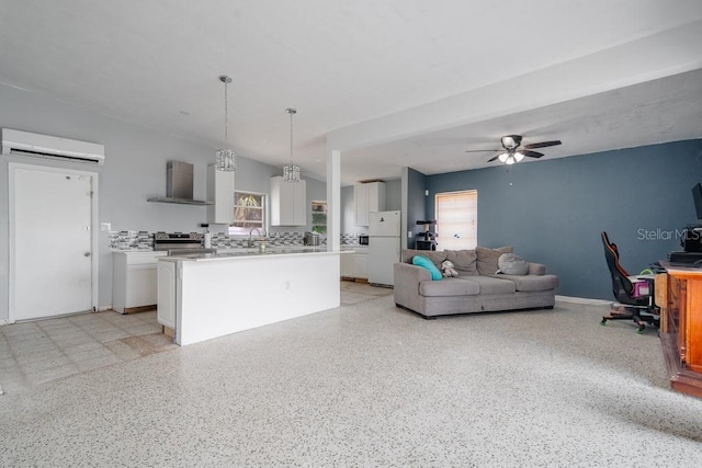 kitchen with hanging light fixtures, stainless steel stove, white fridge, white cabinets, and wall chimney range hood