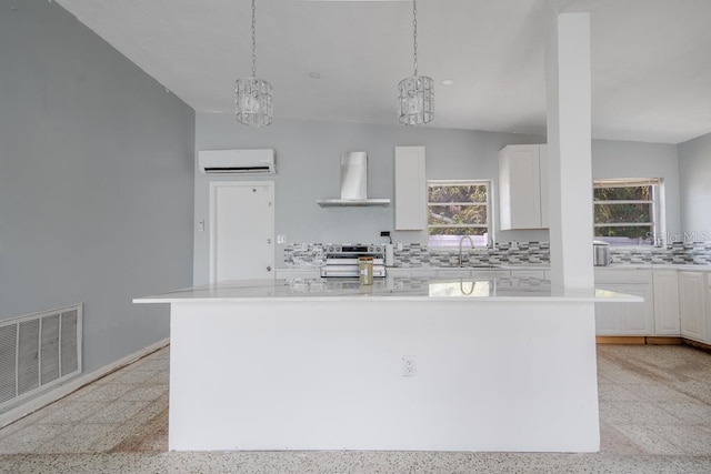 kitchen with wall chimney exhaust hood, a wall mounted AC, a kitchen island, and white cabinets