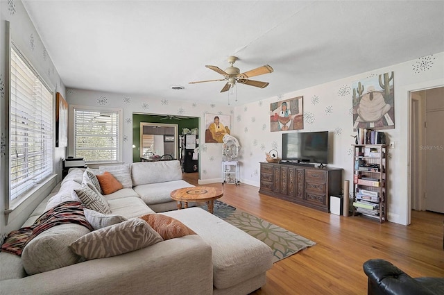 living room featuring wallpapered walls, baseboards, a ceiling fan, and wood finished floors