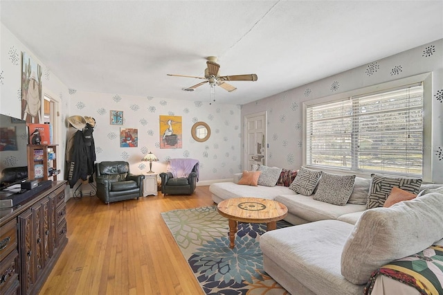 living area with light wood-type flooring, wallpapered walls, ceiling fan, and baseboards