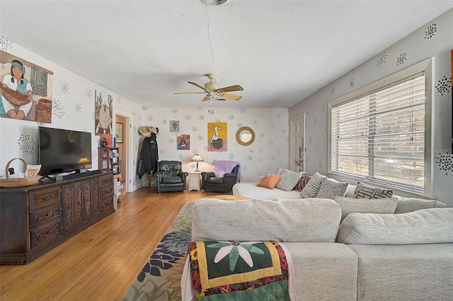 living room with light wood-style floors, a ceiling fan, and wallpapered walls